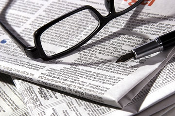 a newspaper, with reading glasses and fountain pen